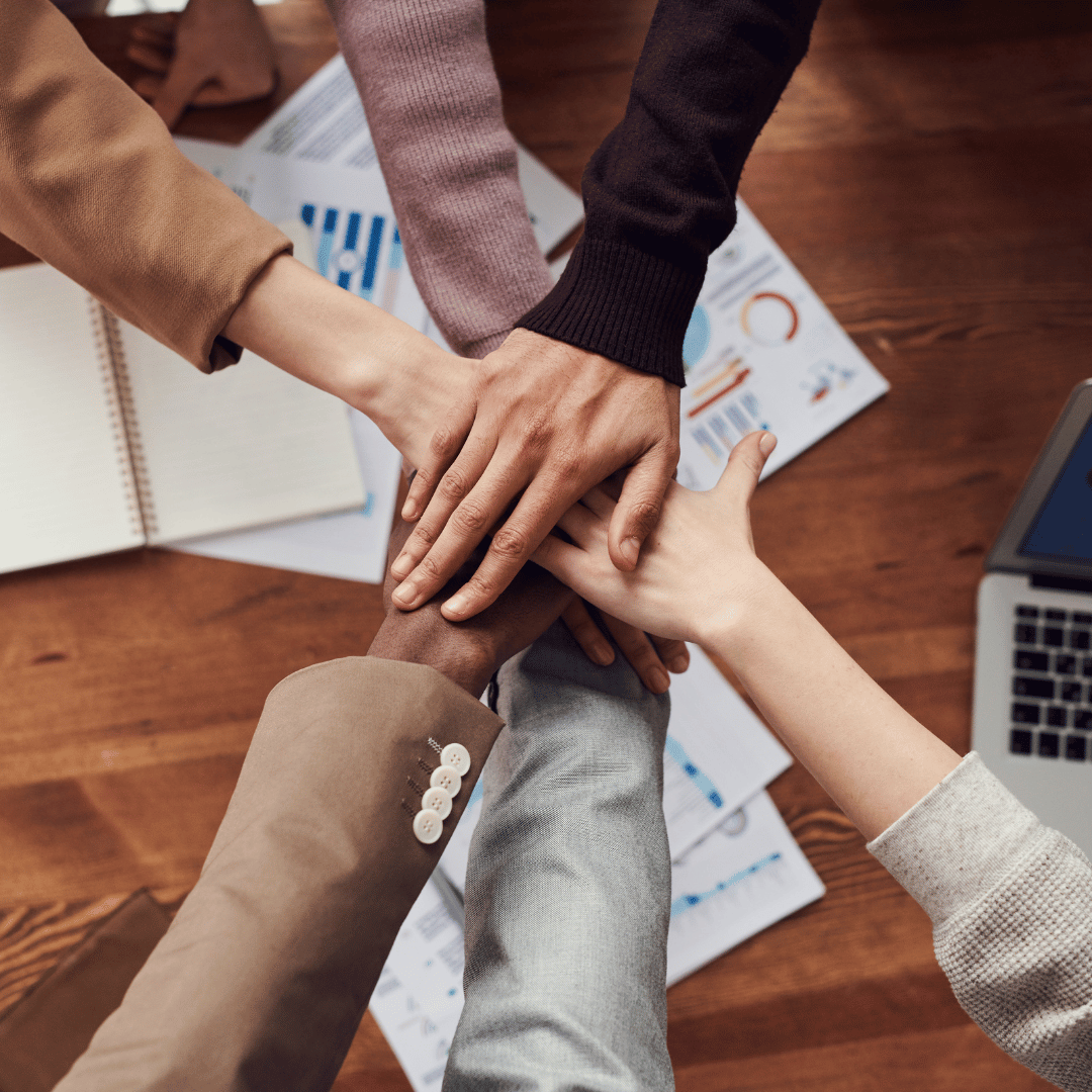 A diverse group of professionals joins hands over a table.