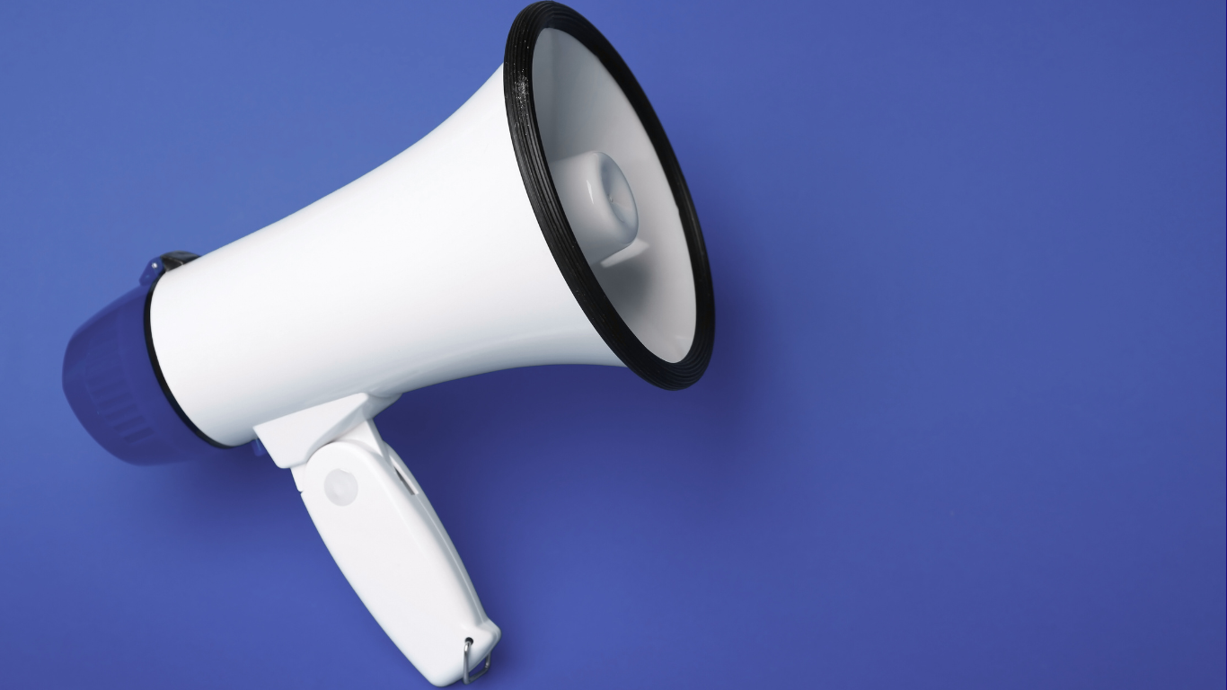 A person wearing a red shirt is holding a button with the word volunteer on it.